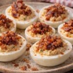 deviled eggs topped with crispy bacon and paprika on a plate