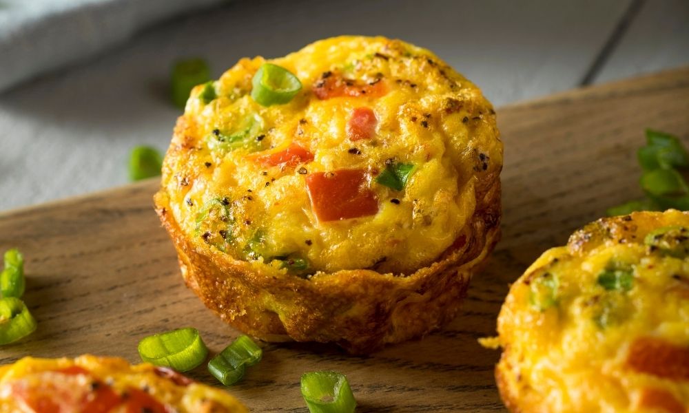 Baked egg omelet muffins with chopped vegetables and green onions on a wooden board, perfect for a quick breakfast or meal prep idea