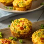 Baked egg omelet muffins with chopped vegetables and green onions on a wooden board, perfect for a quick breakfast or meal prep idea