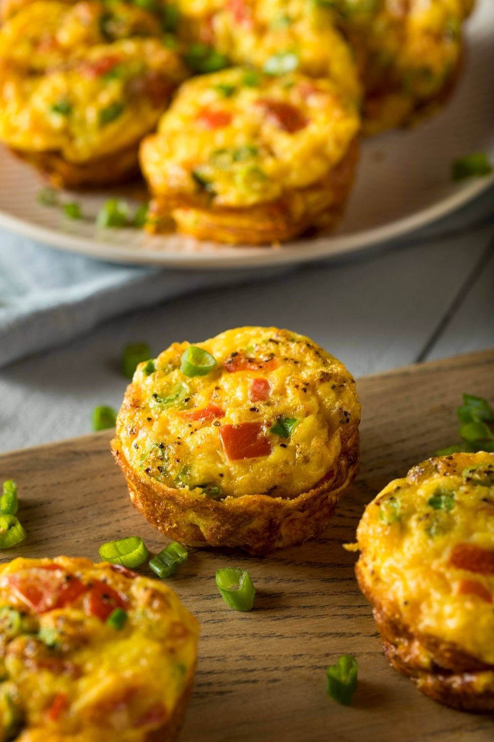 Baked egg omelet muffins with chopped vegetables and green onions on a wooden board, perfect for a quick breakfast or meal prep idea