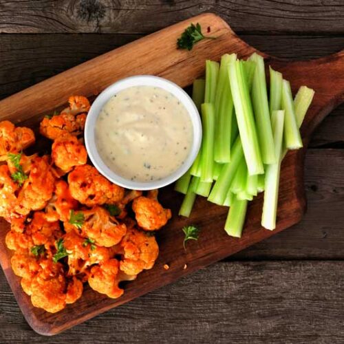 Cauliflower buffalo wings with celery and ranch dip. Top view on a wood paddle board. Healthy eating, plant based meat substitute concept.