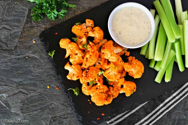 Cauliflower buffalo wings with celery and ranch dip. Top view with a dark slate background. Healthy eating, plant based meat substitute concept.