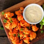 Cauliflower buffalo wings with celery and ranch dip. Top view with a dark slate background. Healthy eating, plant based meat substitute concept.