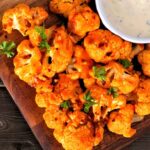 Cauliflower buffalo wings. Top view table scene against a wood background with copy space. Healthy eating, plant based meat substitute concept.