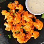 Cauliflower buffalo wings with celery and ranch dip. Top view with a dark slate background. Healthy eating, plant based meat substitute concept.