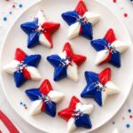 Red, white, and blue candy stars topped with patriotic sprinkles arranged on a white plate for a festive 4th of July dessert