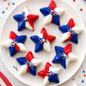 Red, white, and blue candy stars topped with patriotic sprinkles arranged on a white plate for a festive 4th of July dessert