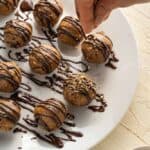 pecan pie truffles rolled into balls on a white plate with chocolate drizzle and pecans sprinkled on top