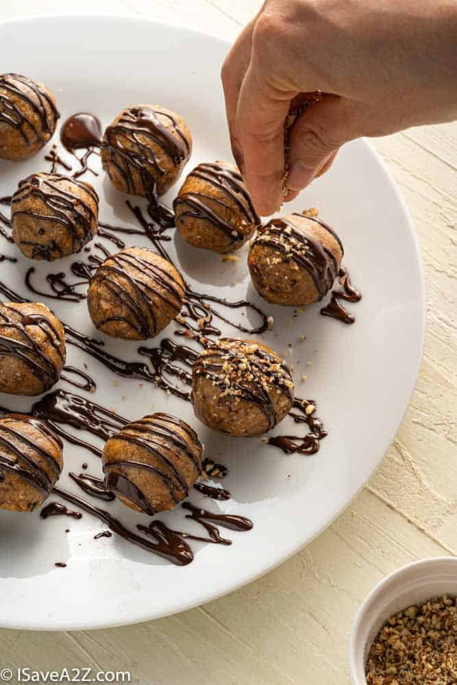 pecan pie truffles rolled into balls on a white plate with chocolate drizzle and pecans sprinkled on top