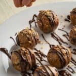 pecan pie truffles rolled into balls on a white plate with chocolate drizzle and pecans sprinkled on top ready to eat