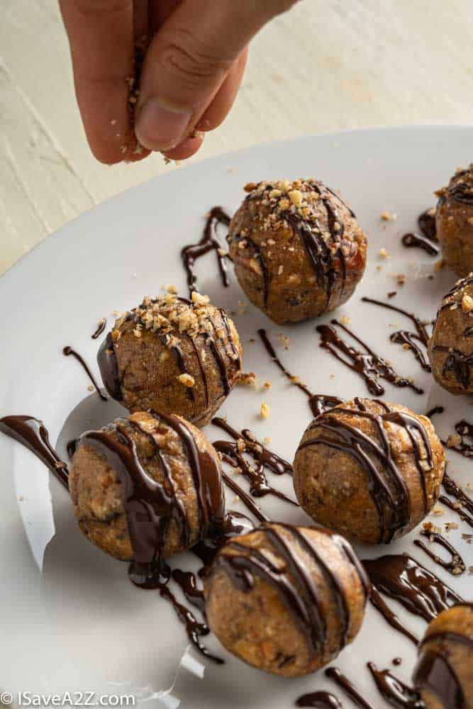 pecan pie truffles rolled into balls on a white plate with chocolate drizzle and pecans sprinkled on top ready to eat